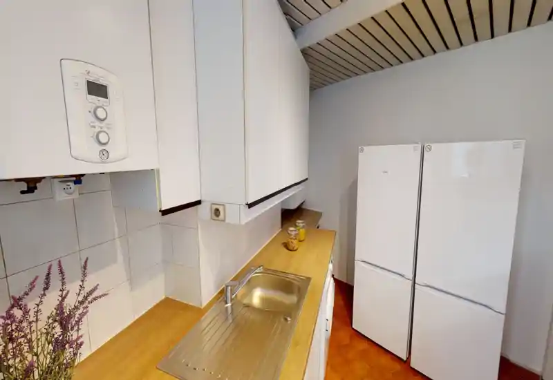 Compact kitchen with a wooden countertop, stainless steel sink and upper white cabinets; two white refrigerators are visible, and decorative jars add a homely touch.