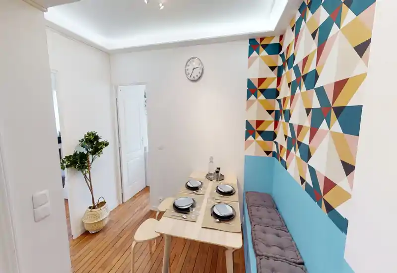 Bright, well-styled dining nook with a set table, bench seating and a colorful geometric feature wall that adds personality to the small space.