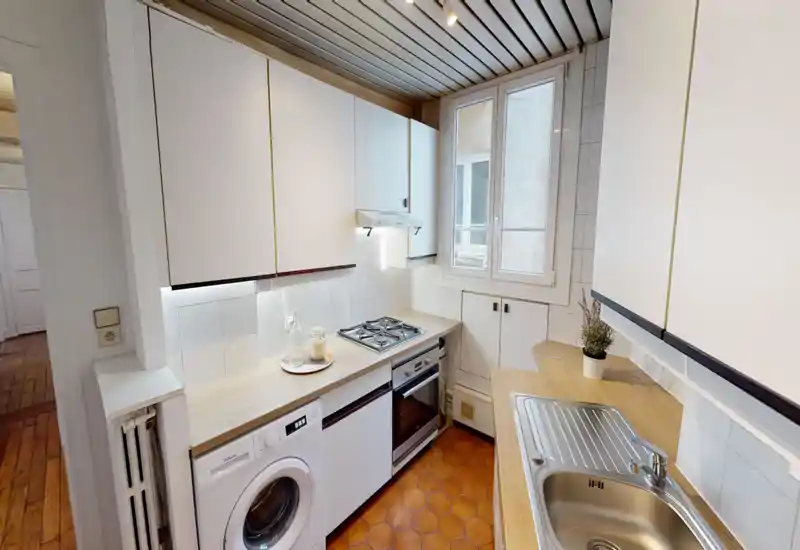 Cucina compatta e ben attrezzata con piano cottura a gas, forno incassato, lavatrice e lavello in acciaio inox. Finestra luminosa e piani in legno chiaro rendono lo spazio ordinato e funzionale, ideale per appartamenti in città.