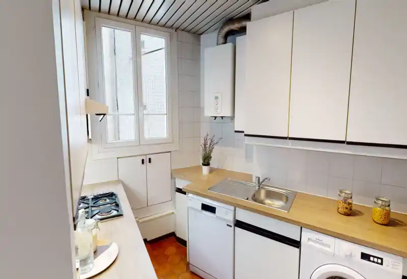 Compact, well-lit galley kitchen with wooden countertops, integrated sink, gas hob and white cabinetry — a tidy, functional cooking space with a window for natural light.