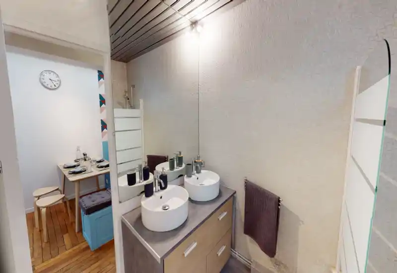 Modern bathroom with double vessel sinks, a large mirror and towel rail; neutral textured walls and soft overhead lighting create a clean, functional space.