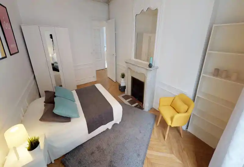 Bright, stylish bedroom with a large bed, soft textiles and a decorative fireplace. Clean white walls, wooden herringbone floor and a cozy rug create a warm, inviting space.