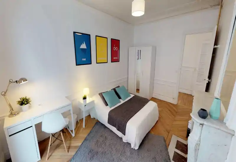 Bright, stylish bedroom with a double bed, bedside table and desk. White walls, wooden herringbone floor and framed prints create a clean, modern feel.