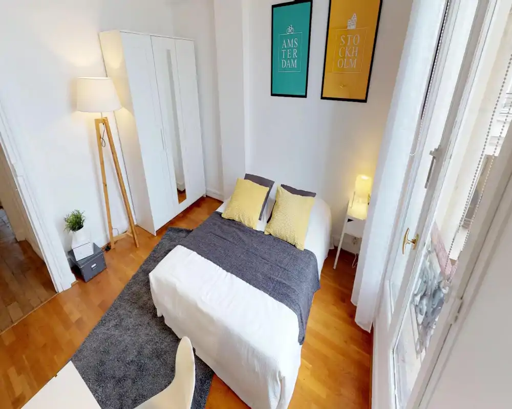 Camera da letto luminosa e curata con letto matrimoniale al centro, cuscini gialli, coperta grigia e armadio; la luce naturale dalla finestra crea un'atmosfera accogliente.