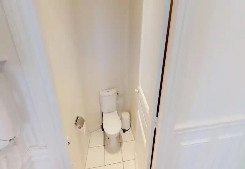 Compact private bathroom with a white ceramic toilet, tiled floor and neutral walls. Small bin and toilet roll holder visible; bright, clean and functional space.