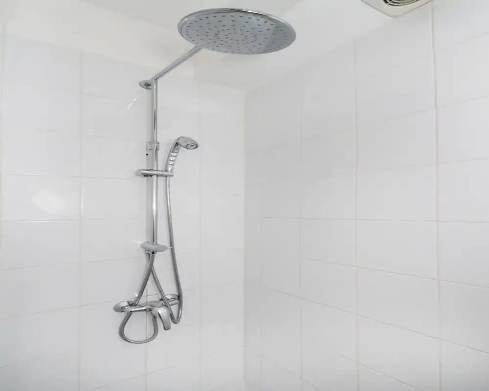 Area doccia moderna e pulita con piastrelle bianche e soffione a pioggia cromato con doccetta a mano.