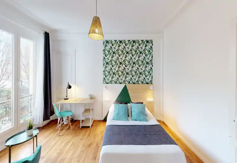 Camera da letto luminosa e moderna con letto matrimoniale, cuscini decorativi e pannello testiera con motivo fogliame. Ampie finestre offrono molta luce naturale e una scrivania vicino alla finestra crea un comodo spazio di lavoro.