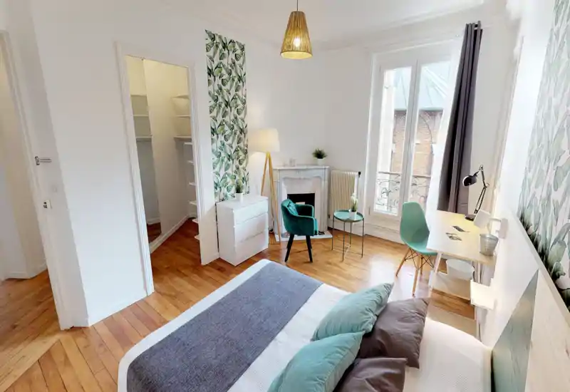 Camera da letto luminosa e stilosa con grande letto in primo piano, pavimento in legno, pannello decorativo, piccolo angolo salotto e scrivania vicino alla finestra — perfetta per soggiorni confortevoli.