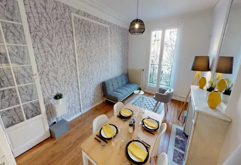 Soggiorno luminoso e di stile con divano compatto, poltrona e tavolo da pranzo apparecchiato per quattro; grande finestra e arredi coordinati rendono lo spazio accogliente e moderno.