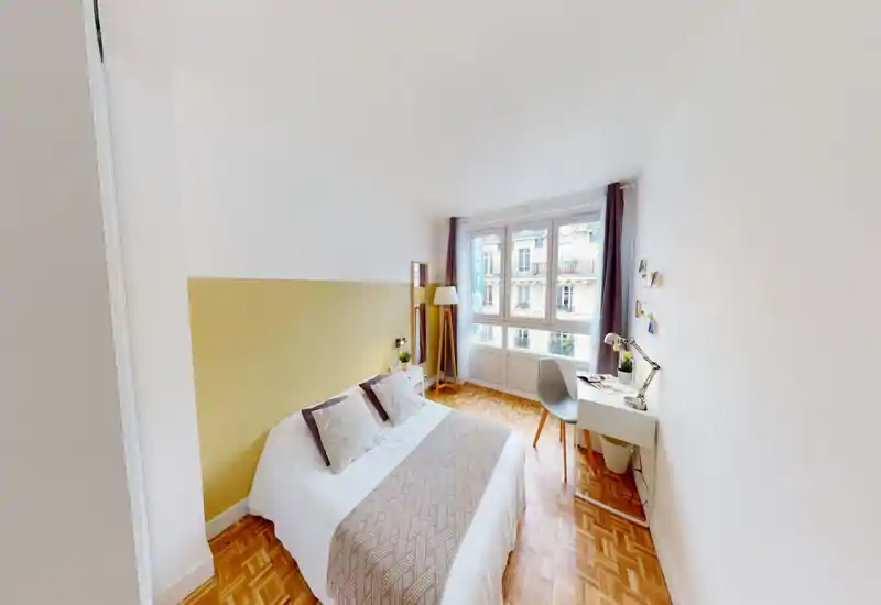 Camera da letto luminosa e accogliente con letto matrimoniale, cuscini decorativi e una scrivania vicino alla finestra; grandi finestre e pavimento in parquet caldo.