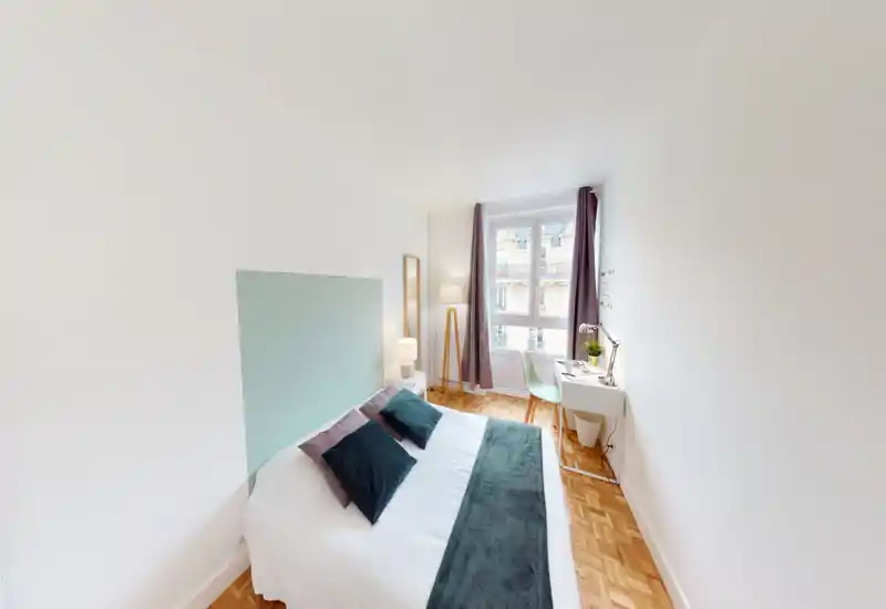 Bright, neatly staged bedroom with a double bed, decorative pillows and a cozy throw. A large window fills the room with natural light and a small desk by the window provides a work nook.