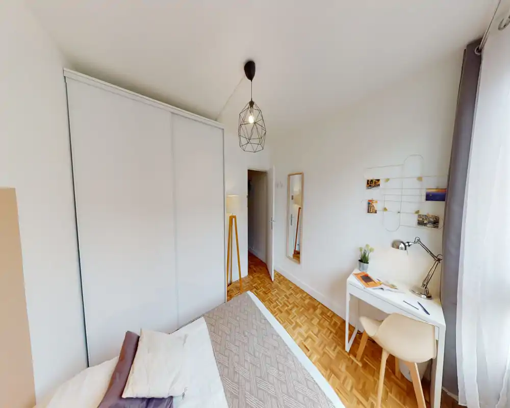 Bright, modern bedroom with a neatly made double bed, built-in sliding wardrobe and a small workspace by the window. Clean parquet floors, soft textiles and tasteful lighting create a calm, inviting atmosphere ideal for a rental listing.