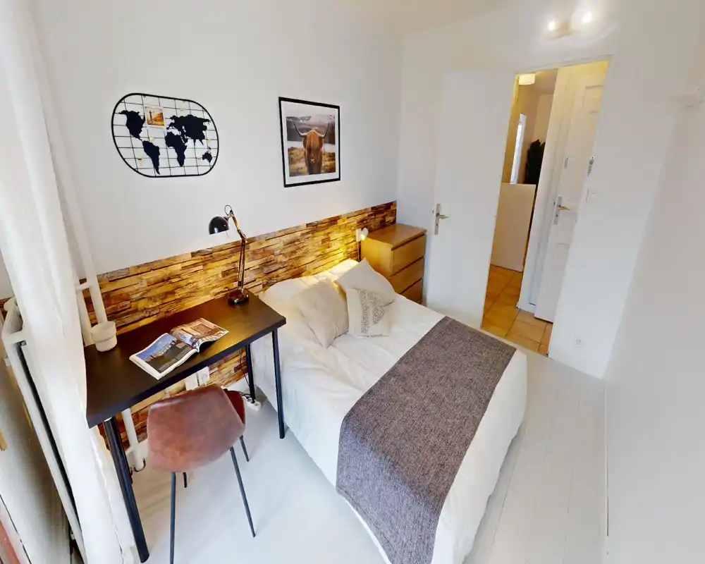 Chambre lumineuse et bien mise en scène avec un lit double confortable, une commode et un petit espace de travail près de la fenêtre. L'accent bois derrière le lit et les textiles doux créent une ambiance chaleureuse et accueillante, idéale pour une annonce.