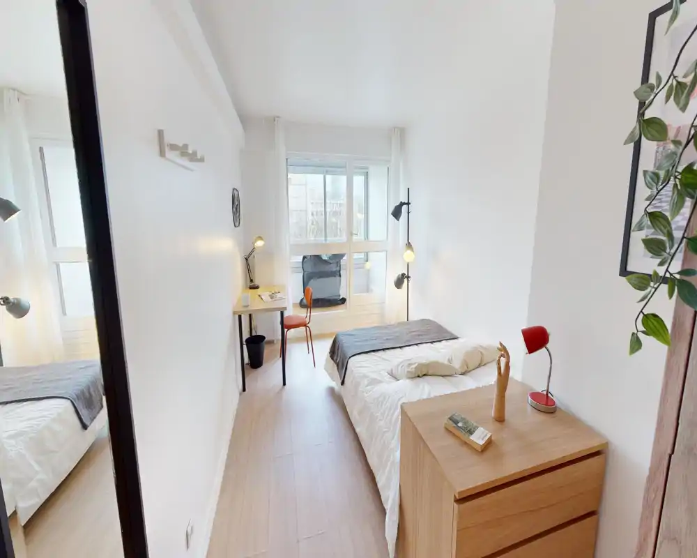 Chambre lumineuse et minimaliste avec lit double, commode en bois, bureau près de la fenêtre et lampes de lecture — parfaite pour un séjour calme et lumineux.