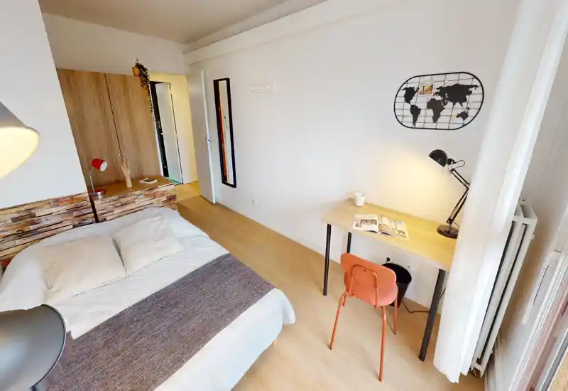 Bright, tidy bedroom with a large bed in the foreground, a wooden headboard and a small work desk by the window — ideal for comfortable stays and remote work.