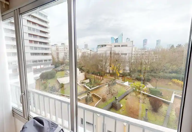 Balcony view overlooking a landscaped courtyard and surrounding buildings, with large sliding windows letting in abundant natural light.