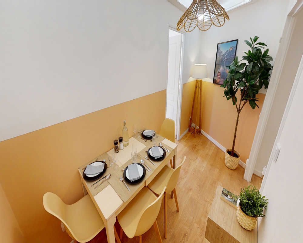 Coin repas aménagé avec une table dressée pour quatre, murs bicolores chauds, sol en bois et plantes décoratives pour une atmosphère conviviale et lumineuse.
