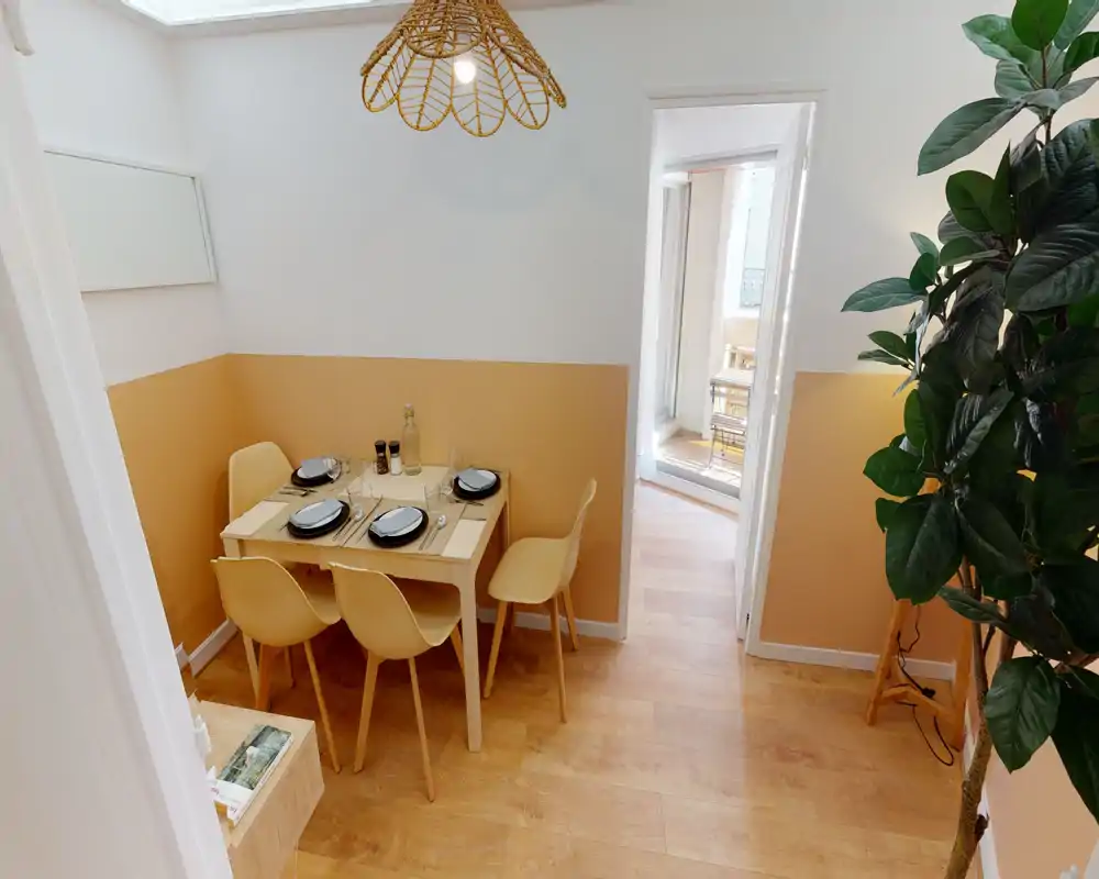 Coin repas lumineux et chaleureux avec une table pour quatre dressée, une suspension et un sol en bois qui créent une ambiance accueillante.