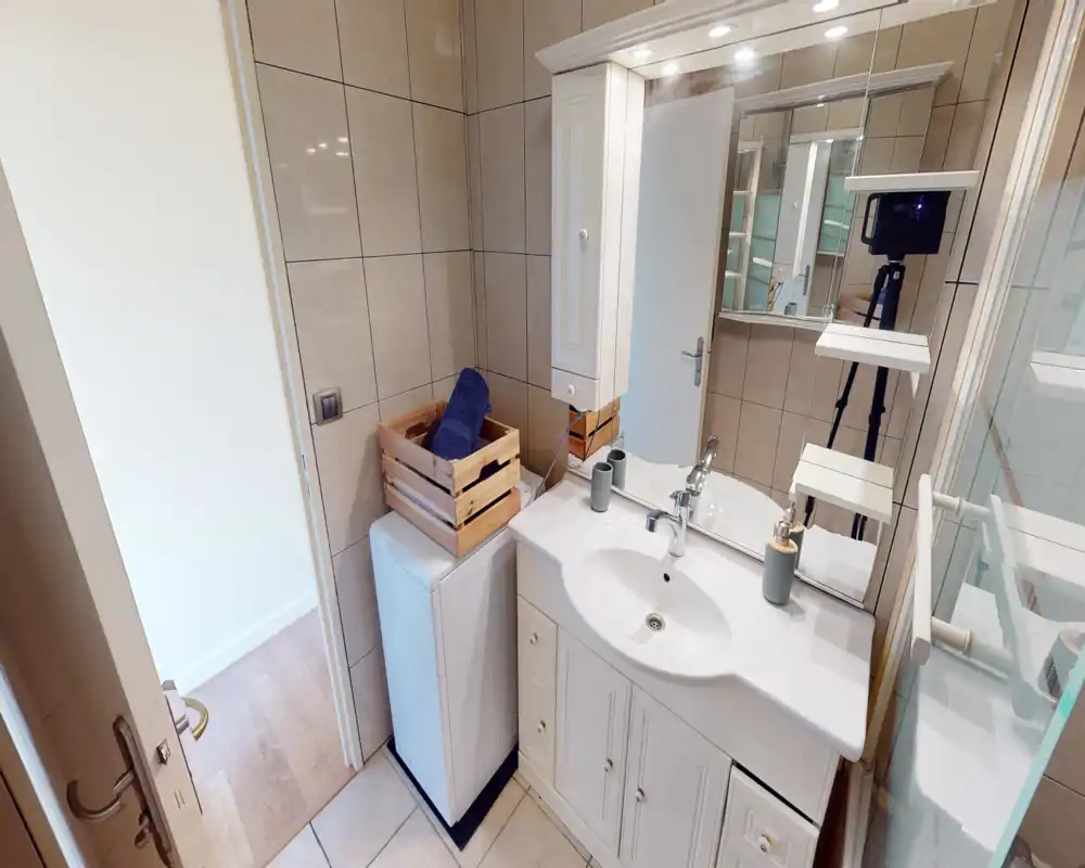 Petite salle de bains moderne avec murs carrelés, meuble-lavabo blanc, miroir et étagères; lumineuse, propre et bien mise en scène.