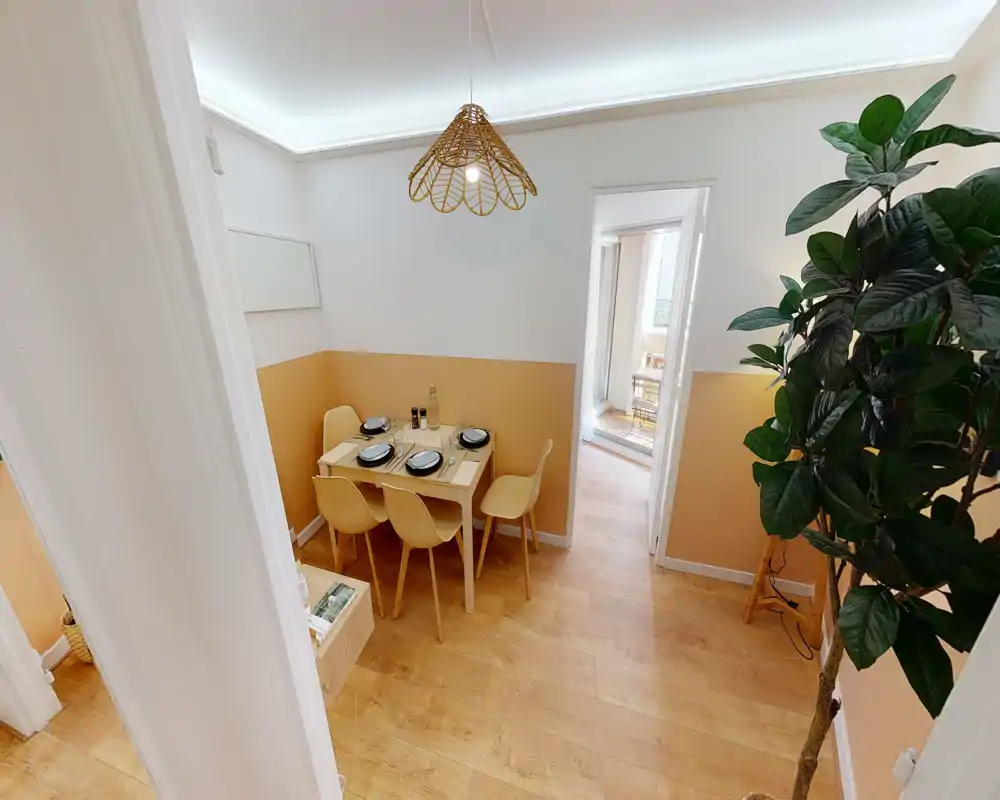 Coin repas lumineux et chaleureux avec une petite table dressée pour quatre, chaises modernes et suspension décorative—idéal pour des repas conviviaux.