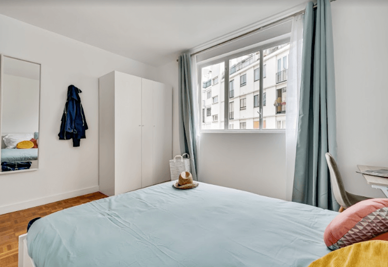 Chambre lumineuse et bien mise en scène avec un grand lit au premier plan, une armoire et une fenêtre apportant la lumière naturelle — idéale pour les annonces.