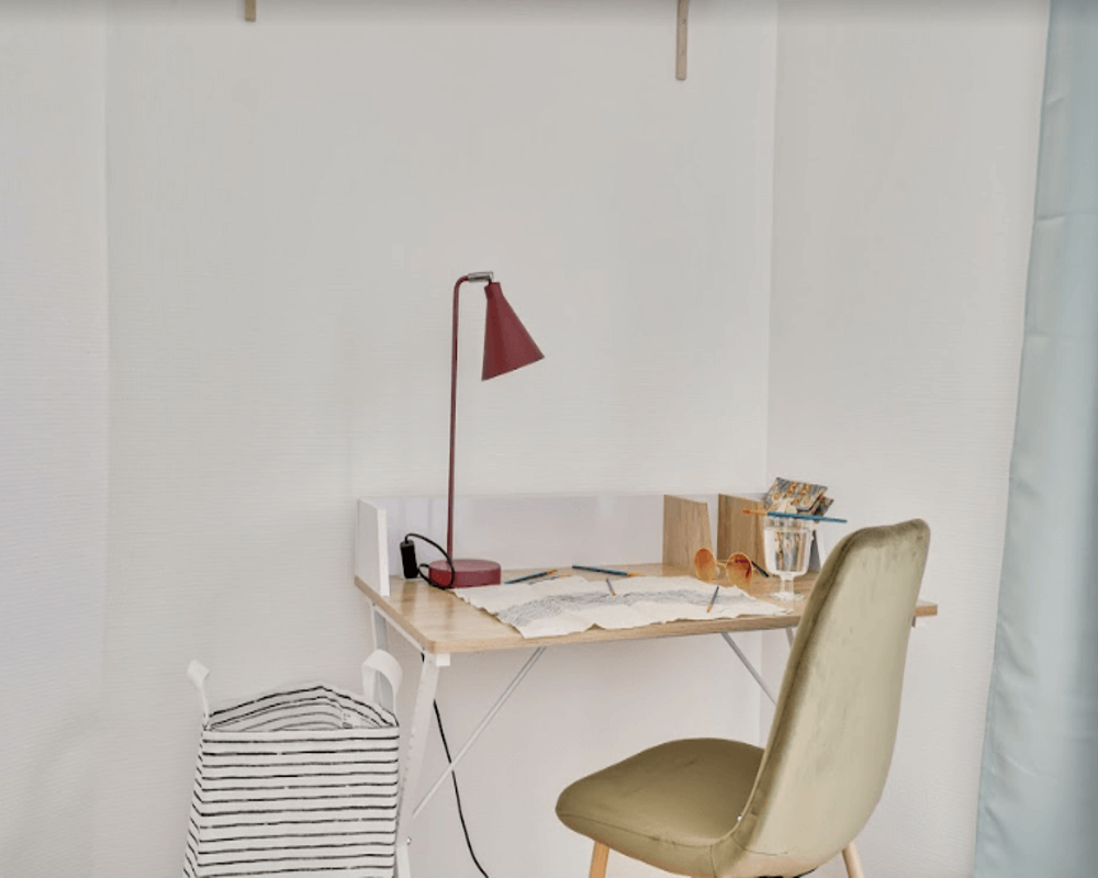 Compact workspace corner with a small wooden desk, task lamp and a comfortable upholstered chair — bright, tidy and suitable for remote work.