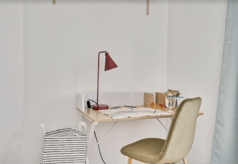 Compact workspace corner with a small wooden desk, task lamp and a comfortable upholstered chair — bright, tidy and suitable for remote work.