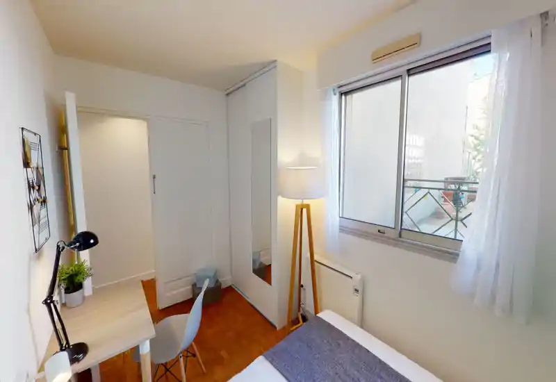 Small, clean bedroom with a single bed by a bright window, a slim wardrobe with mirror, a freestanding lamp and a compact desk — ideal for a student or single occupant.