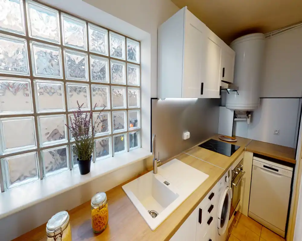 Cuisine moderne et compacte avec plan de travail en bois, évier intégré, plaque à induction et éclairage sous les placards ; bocaux décoratifs et petite plante apportent une touche chaleureuse.