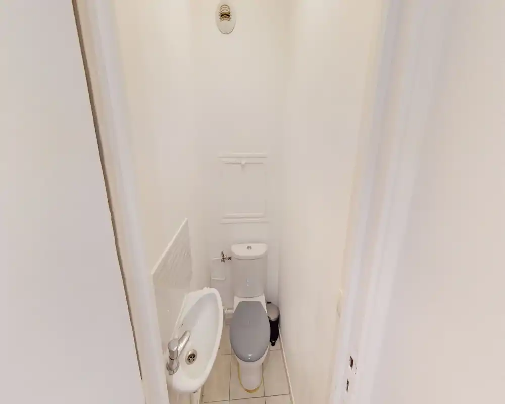 Petite toilette avec lavabo et WC proches dans un espace étroit et lumineux aux murs blancs — parfait pour un WC invité.