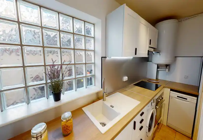 Compact modern kitchen with a wood countertop, integrated sink, induction hob and under-cabinet lighting; decorative jars and a small plant add a warm touch.