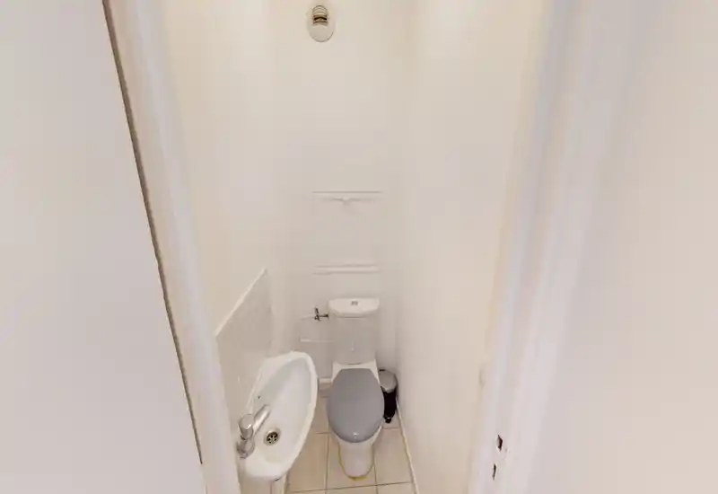 Compact toilet room with a small sink and a close-coupled toilet in a narrow, well-lit white space — ideal for a guest WC.