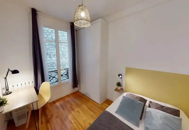 Bright, cozy bedroom with a comfortable double bed, soft pillows and a modern headboard. Large window with curtains brings natural light; a desk and wardrobe complete the functional layout.