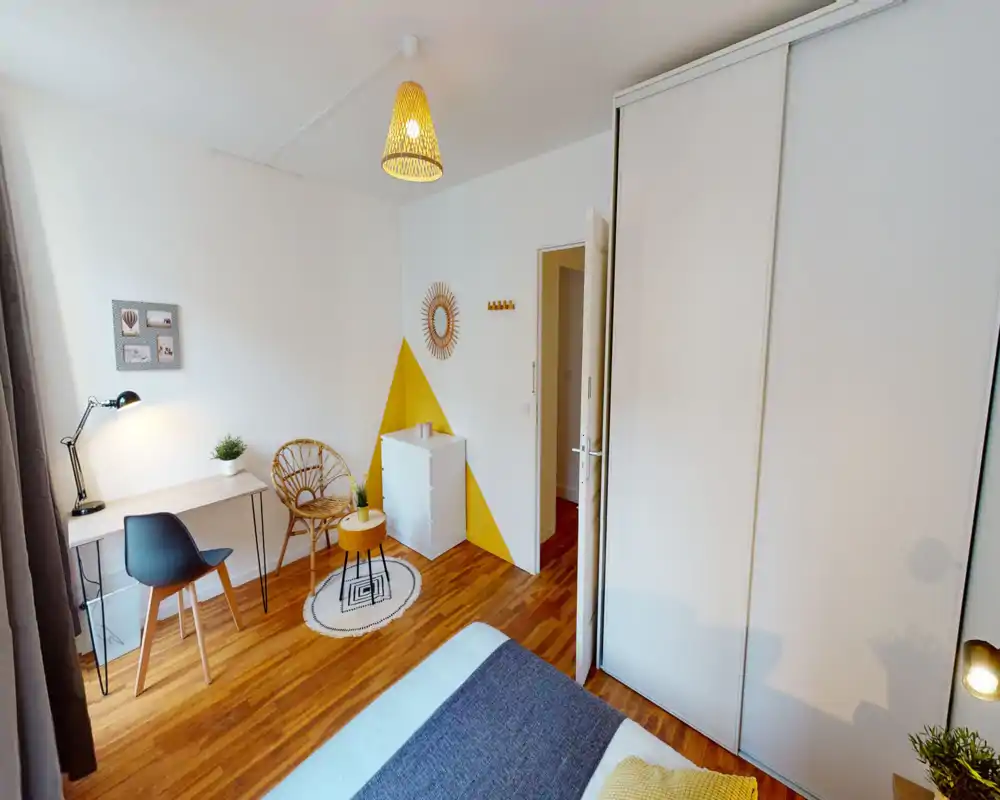 Chambre lumineuse et aménagée avec lit visible au premier plan, parquet, petit bureau et coin détente cosy — parfaite pour une location courte ou une personne seule.
