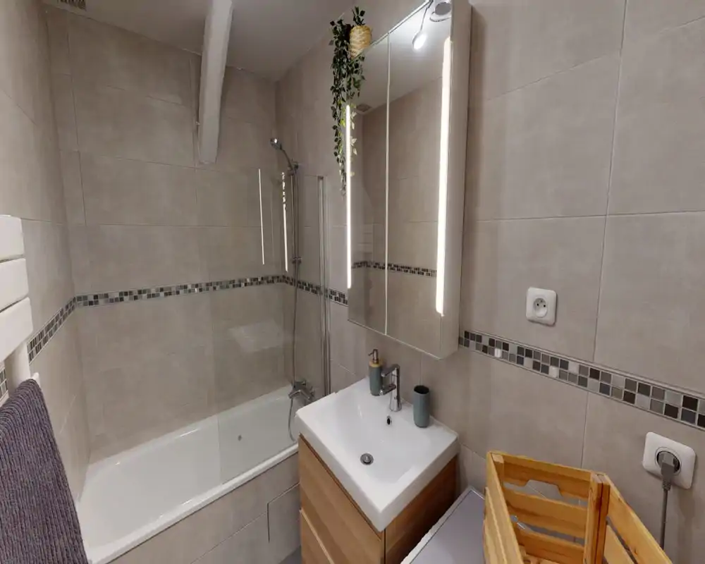 Salle de bain moderne carrelée avec baignoire-douche, meuble vasque avec miroir et tons neutres chaleureux.