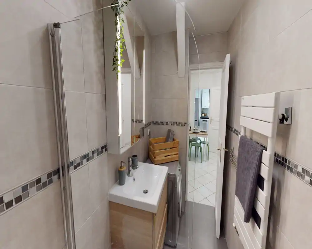 Salle de bain moderne carrelée avec lavabo, armoire miroir, sèche-serviettes et lave-linge ; tons neutres et bonne luminosité.