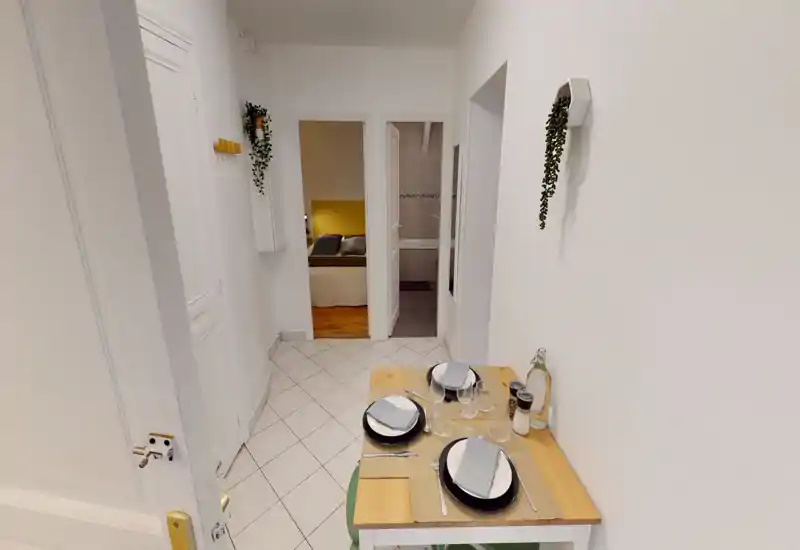 Petit coin repas aménagé avec une table en bois pour deux, vaisselle et verres soigneusement disposés sur des murs blancs immaculés — idéal pour un appartement compact ou un coin petit-déjeuner.