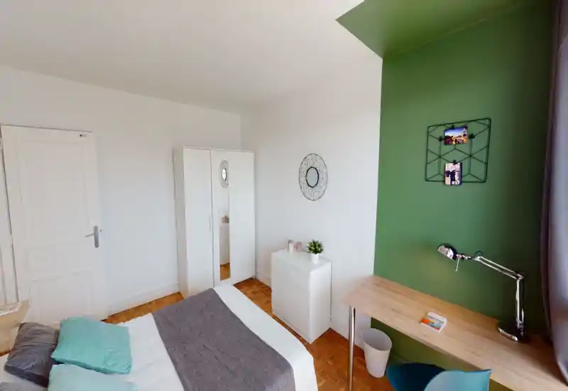 Bright, well-styled bedroom with a large bed, soft textiles and a green accent wall. A wooden desk and tidy storage units make the room practical for work and relaxation.