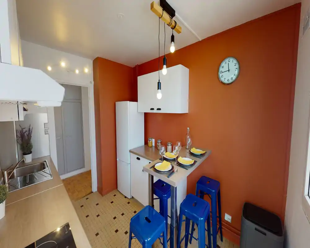 Well-equipped compact kitchen with warm terracotta walls, a fridge, overhead cabinet, sink and a breakfast bar with four stools—bright, styled and ready for casual dining.