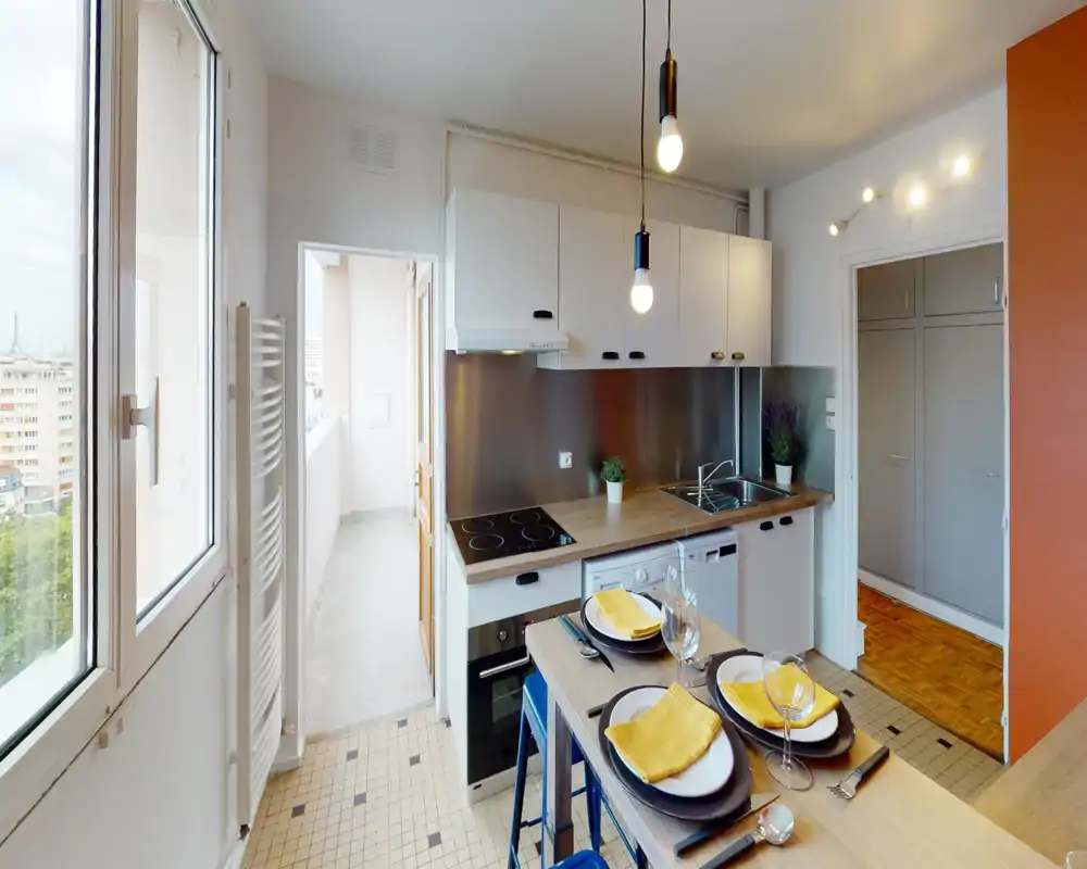 Compact, modern kitchen with a built-in oven, electric hob, sink and breakfast bar set for two; bright natural light from a large window and tasteful decorative touches.