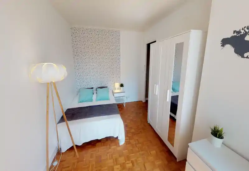 Camera da letto moderna e luminosa con letto matrimoniale in lenzuola bianche, cuscini turchesi e copriletto scuro, parete decorativa, comodino con lampada, lampada da terra e armadio bianco con specchio.