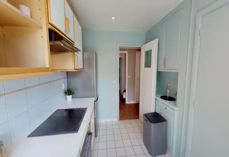 Cucina luminosa e ordinata con mobili pastello, piano cottura elettrico, frigorifero e piani ben organizzati — perfetta per foto di annunci che mostrano un'area cottura moderna e pulita.