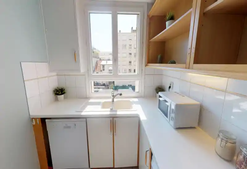 Cucina compatta e luminosa con lavello sotto una grande finestra, mensole in legno a vista e forno a microonde sul piano — ordinata e ben illuminata, ideale per un appartamento cittadino.