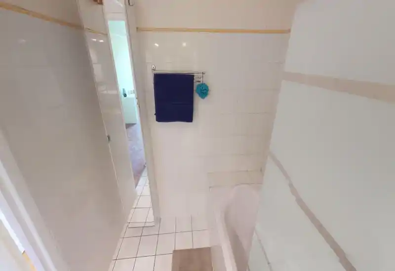 Bagno pulito e luminoso con piastrelle, vasca parzialmente visibile, parete doccia in vetro satinato e un portasciugamani con asciugamano blu scuro.