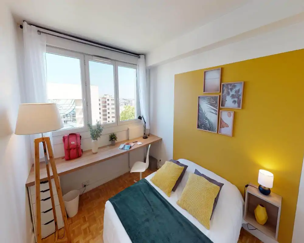 Chambre moderne et lumineuse avec lit double en linge blanc, coussins moutarde et plaid vert foncé ; grande fenêtre, bureau en bois et éléments chaleureux pour un espace accueillant et propice au travail.