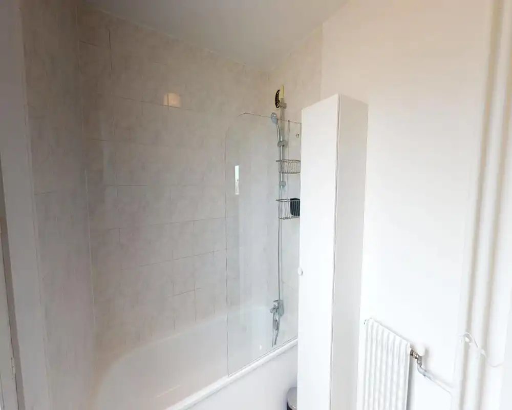 Salle de bain propre et lumineuse avec baignoire et douche à tête; murs carrelés et paroi en verre pour un espace moderne et fonctionnel.