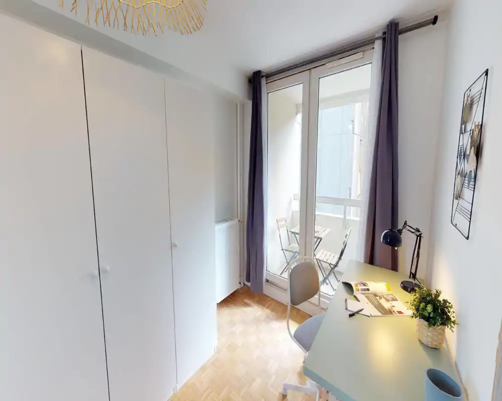 Small bright bedroom corner with a study desk, wardrobe and balcony access; neat parquet flooring and soft curtains create a calm, functional space.