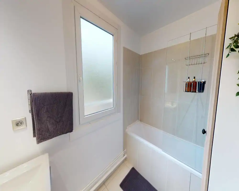 Clean, modern bathroom with a bathtub and tiled walls, frosted window for privacy, and organized toiletries on a hanging rack.