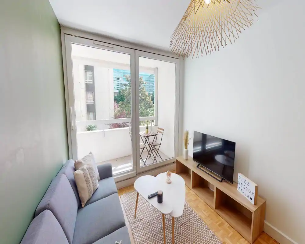 Bright, modern living room with a comfortable sofa, coffee table and TV unit opening onto a small balcony — ideal for relaxing and enjoying natural light.