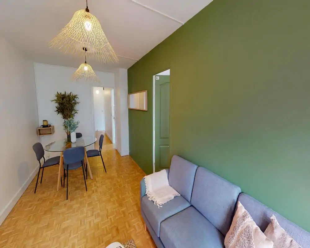 Bright, styled living area with a comfortable grey sofa, decorative cushions and a dining table with chairs under woven pendant lights — modern, cozy space ideal for relaxing and dining.